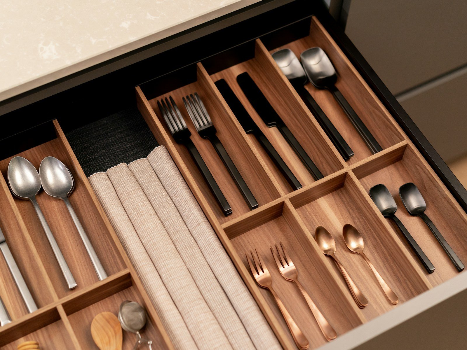 A neatly organised walnut kitchen drawer with cutlery and wooden utensils in dividers