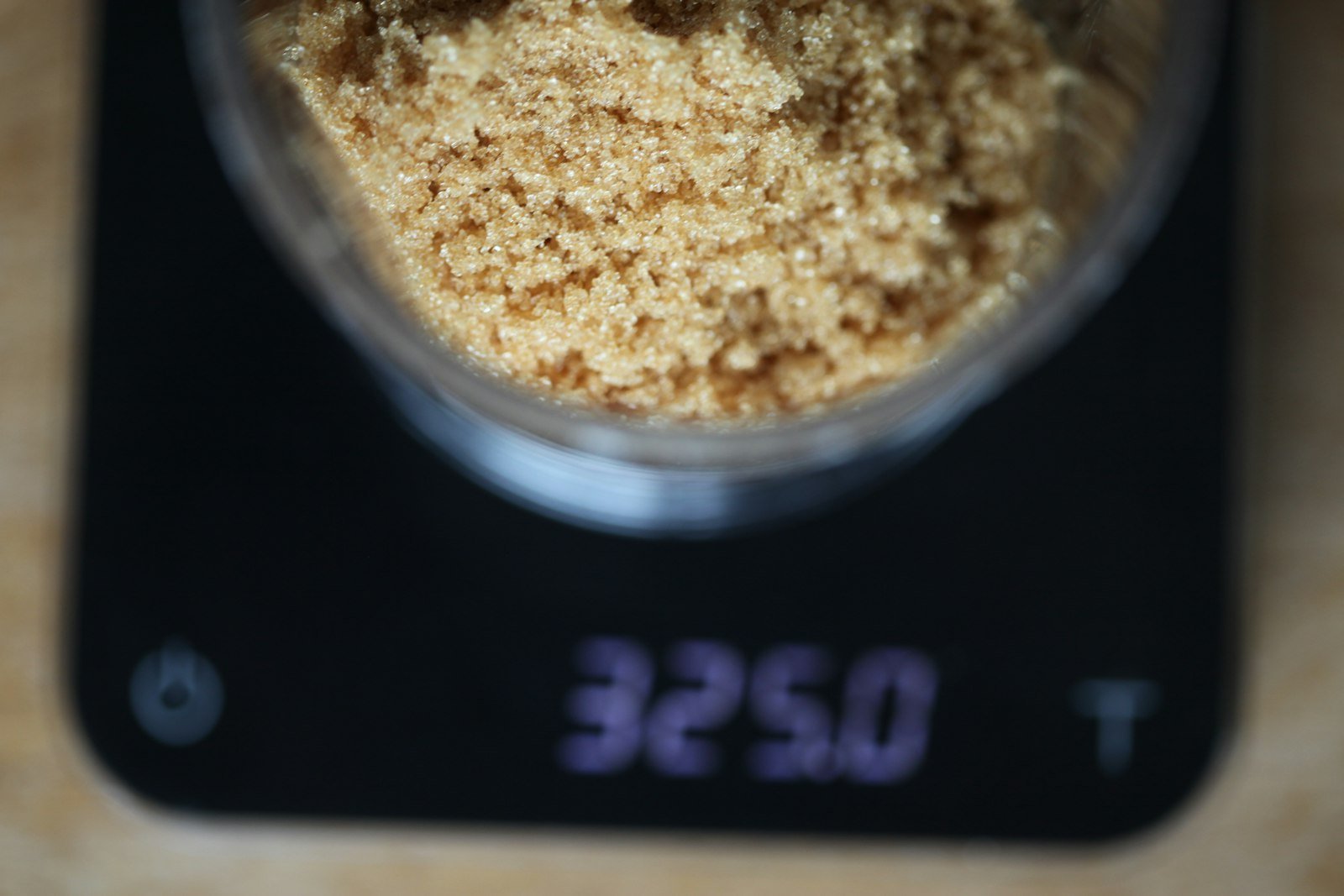 Brown sugar being weighed in a cup on a digital kitchen scale