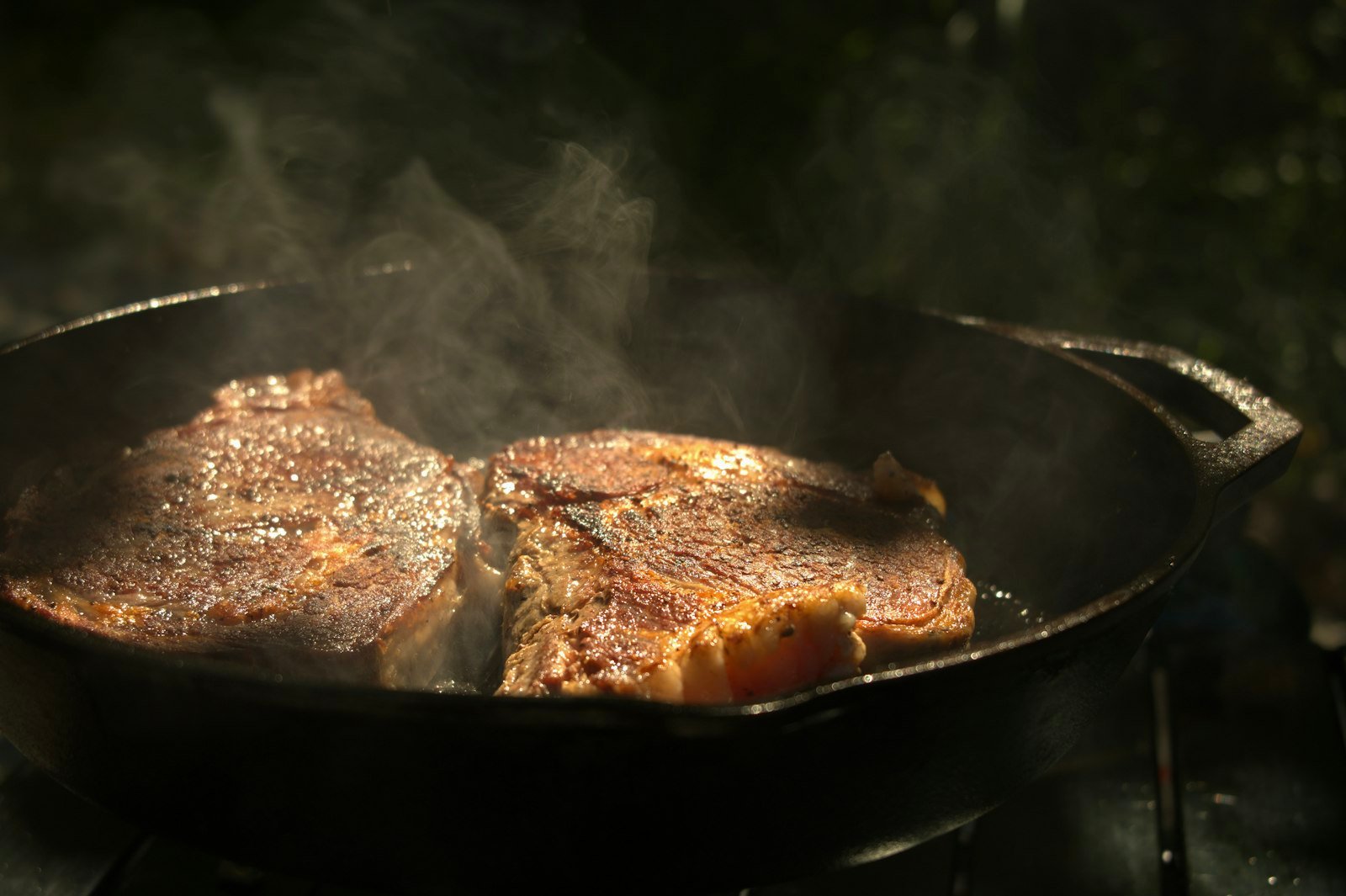 A seasoned cast iron skillet searing a steak on the hob